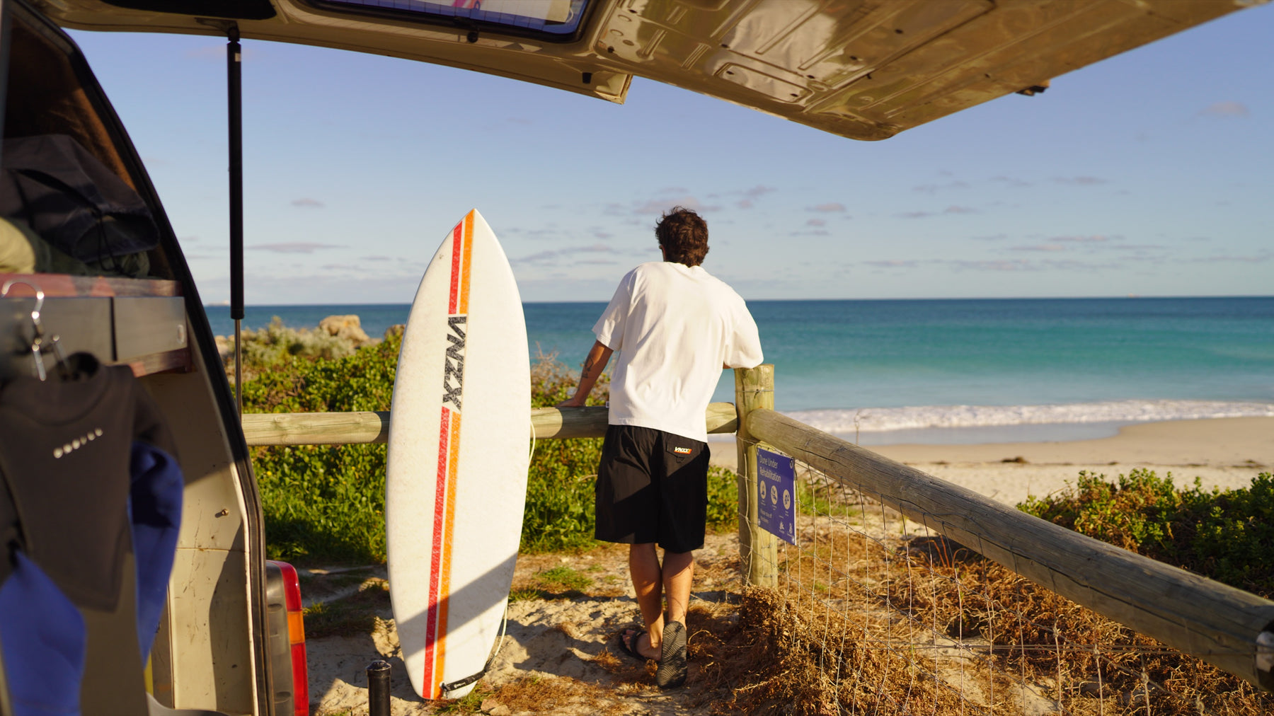 surfboard leaning on a beach fence, looking out from the back of the van