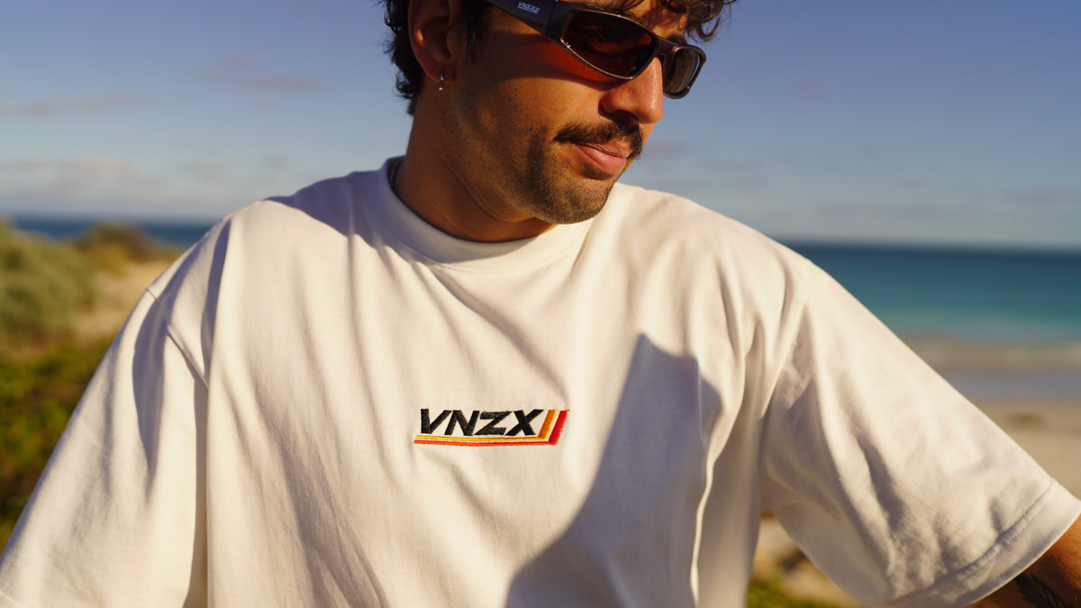 white every day tee with embroidered vnzx logo with the ocean behind
